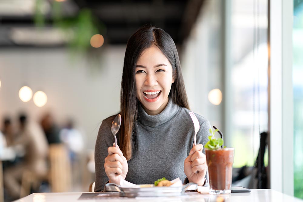 Young attractive asian woman holding fork and spoon feeling hung